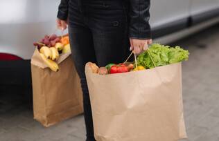 Person carrying brown paper grocery bags leaving Healing Harvest food pantry service for cancer patients.